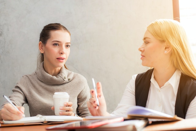 Two people sitting a table chatting over coffee and notes